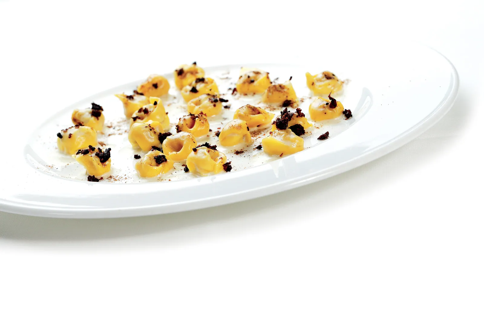 Tortellini tradizionali bolognesi, cacio e pepe di parmigiano reggiano 30 mesi, briciole di olive Taggiasche e polvere di porcini testa nera dell’Appenino Tosco-Emiliano